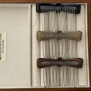 Three colors of matte bow hair combs with metal teeth displayed in a wooden box