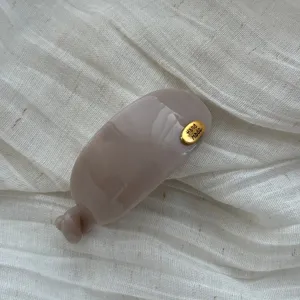 Detailansicht einer minimalistischen ovalen Haarklammer in Taupe mit goldenem Anhänger