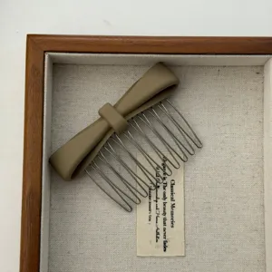 Detail view of a matte khaki bow hair comb presented inside a decorative wooden frame box.