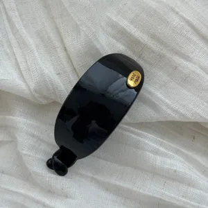 Nahaufnahme der glänzenden schwarzen Haarspange mit goldener Hand made-Plakette.