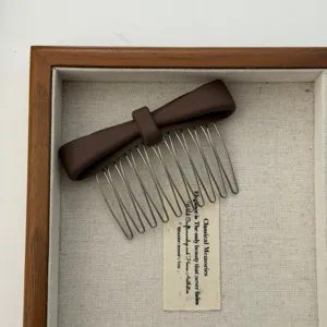 Detailed close-up of a brown matte bow hair comb presented in a rustic wooden jewelry tray
