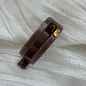 Detailansicht einer glänzend braunen Bananen-Haarklammer mit einem goldenen Etikett