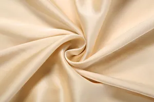 Close-up of smooth champagne silk satin fabric showcasing elegant glossy texture details.