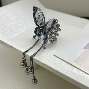 Detailed shot of a metal butterfly hair clip with blue rhinestones and dangling grey pearls.