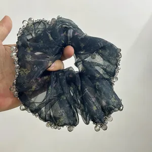 Dettaglio di uno scrunchie in organza floreale scura con bordo di perline in mano.