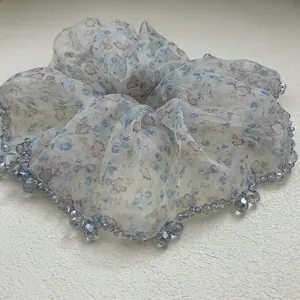 Dettaglio di uno scrunchie in organza a fiori con bordi decorati con perle blu