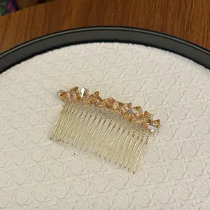 Macro detail of elegant champagne crystal hair comb featuring golden metal prongs and facets.