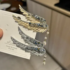 Close-up of angel wing hair clips with blue crystals and pearl tassels on display card.