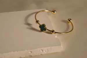 Gold open cuff bracelet detail showcasing green clover and bead charms on textured block