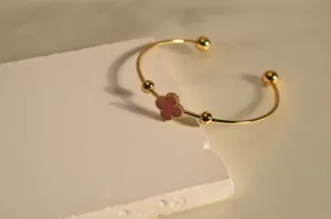 Gold stainless steel open cuff bracelet detail view with pink clover charm and bead accents.