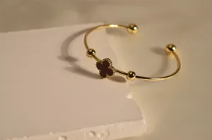 Elegant stainless steel gold open cuff bracelet featuring a chic red four-leaf clover charm.