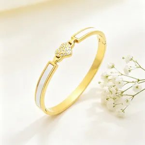 Bracelet en acier titane doré avec pendentif cœur en strass et détails en émail blanc.