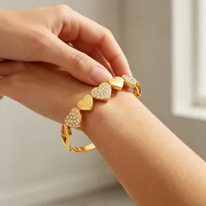 Gros plan de détail du bracelet cœur doré avec des strass scintillants sur le poignet.