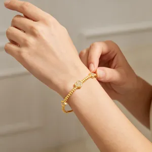 Détail du bracelet en acier titane doré avec pendentif cœur et perles porté au poignet.