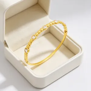 Vue rapprochée détaillée du jonc en acier titane doré avec strass en cœur dans un écrin.