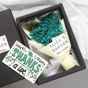 Primer plano de una tarjeta 'THANKS a lot' con flores secas en una caja de regalo negra