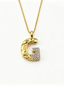 Nahaufnahme des goldenen Buchstaben G Anhängers mit Kristallen und geschmolzener Metallstruktur.