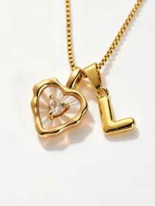 Close-up detail shot of a gold-toned necklace featuring a mother-of-pearl heart and letter L.