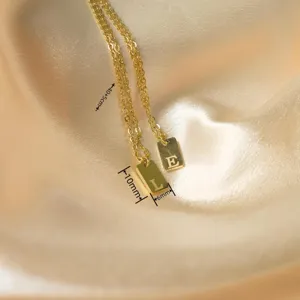 Detail shot of golden stainless steel square pendant necklace with engraved letter charms.