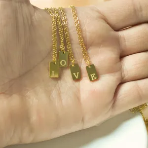 Detail shot of gold chain necklaces with engraved letter tags spelling love held in hand.