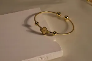 Closeup view of a gold-plated open cuff bracelet featuring a chic clover motif and polished beads.