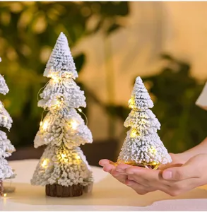 Macro detail of mini flocked Christmas tree with warm LED lights held in person's hands