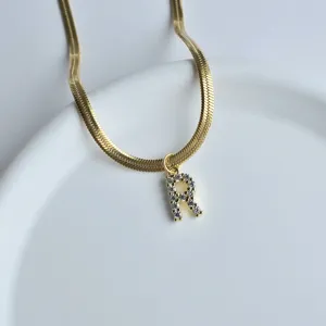 Gold flat snake chain necklace with sparkling crystal letter R pendant detail close up.