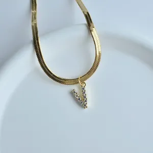 Close-up of a gold flat herringbone chain necklace featuring a sparkling zircon V letter pendant.