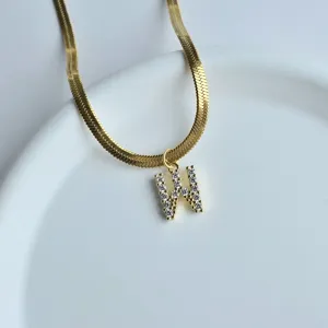 Detail shot of gold herringbone chain necklace with rhinestone letter W pendant chic.