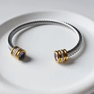 Detailansicht eines Edelstahl-Kabelarmbands mit goldenen Endkappen und lila Steinen.