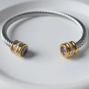 Nahaufnahme des Edelstahl-Kabelarmbands mit lila Stein und Kristallen auf weißem Teller.