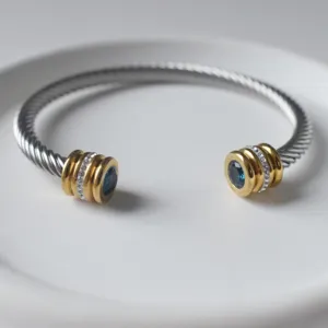 Detailaufnahme eines Edelstahldraht-Armreifs mit blauem Stein und funkelnden Strass-Goldkappen.