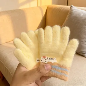 Close-up view of fluffy yellow knit gloves featuring cute bear badge for winter warmth.