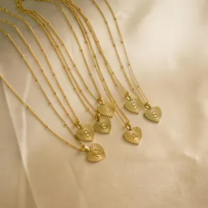 Detailed shot of stainless steel initial heart necklace with sunburst texture and delicate chain.