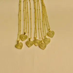 Detailed view of gold stainless steel sunray heart necklaces with engraved alphabet letter pendants.