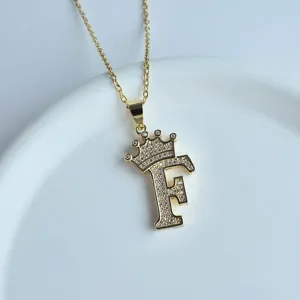 Vue en gros plan d'un collier pendentif lettre F couronne en or avec des pierres étincelantes.