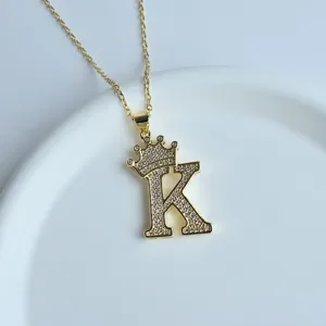 Gros plan d'un collier lettre K en or avec pendentif couronne micro-serti de strass.