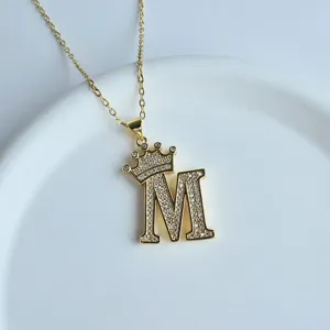 Gros plan sur le collier pendentif lettre M couronne dorée aux détails étincelants
