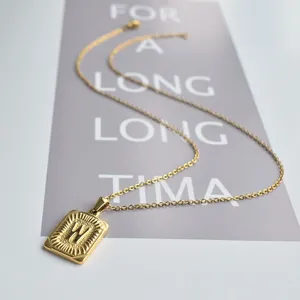 Detail shot of a gold stainless steel square letter W pendant necklace on grey card prop.