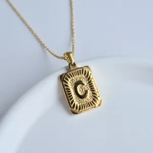 Close-up of golden rectangular initial letter C pendant necklace with sunburst texture.