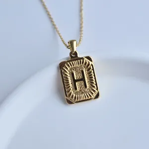 Close-up of gold rectangular initial pendant necklace with letter H detail on white dish.