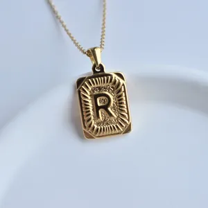 Close-up detail of a gold stainless steel square letter R pendant necklace on white dish.