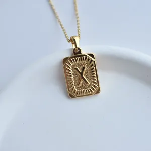 Gold stainless steel square pendant necklace detail shot featuring embossed letter X design.