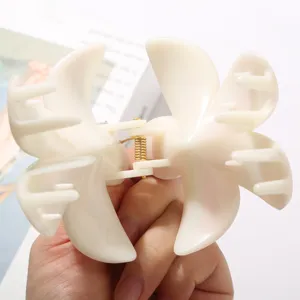 Primer plano detallado de una pinza para el cabello floral blanco crema con resorte dorado.