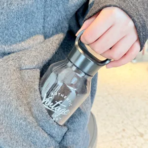 Hand legt eine tragbare Tritan-Wasserflasche mit Griff in eine graue Manteltasche