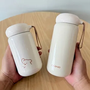 Nahaufnahme von zwei cremeweißen, pilzförmigen Thermo-Trinkflaschen mit süßem Bären-Design.