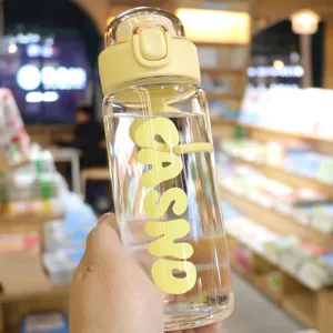 Close-up view of a transparent glass water bottle with yellow bounce lid and brand logo