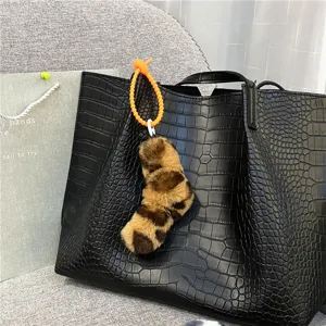 Close-up of a trendy leopard print plush twisted charm attached to a black crocodile bag