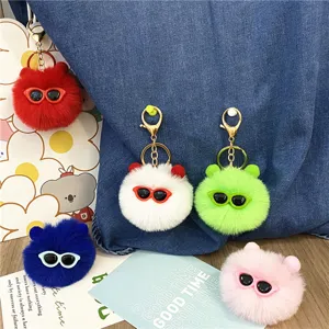 Variety of colorful cute fluffy monster pompom keychains with sunglasses on a denim bag
