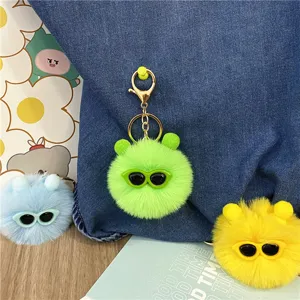 Detail shot of cute fuzzy plush ball keychains with glasses attached to a denim bag